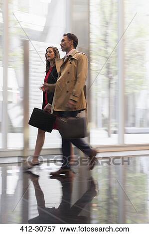 Stock Photo - Corporate businessman and businesswoman walking and talking in corridor. Fotosearch