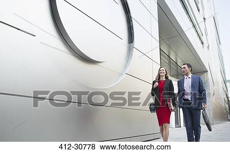 Stock Photo - Corporate businessman and businesswoman walking outside modern building. Fotosearch