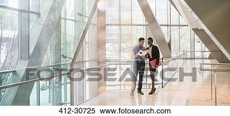Corporate businessman and businesswoman discussing paperwork in modern lobby View Large Photo Image Stock Photography - Corporate businessman and businesswoman discussing paperwork in modern lobby. Fotosearch