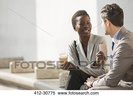 Stock Photography - Corporate businessman and businesswoman with coffee and cell phone talking on bench. Fotosearch