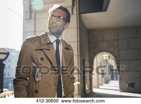 Stock Image - Corporate businessman in trench coat standing in sunny cloister. Fotosearch