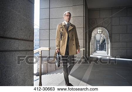 Corporate businessman in trench coat walking in cloister View Large Photo Image Stock Image - Corporate businessman in trench coat walking in cloister. Fotosearch