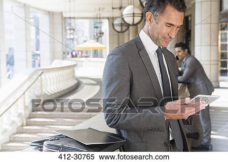 Stock Photography - Corporate businessman using digital tablet outdoors. Fotosearch
