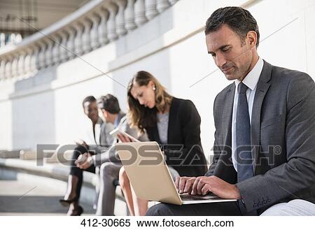 Corporate businessman using laptop on bench outdoors View Large Photo Image Stock Photography - Corporate businessman using laptop on bench outdoors. Fotosearch