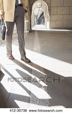 Stock Photo - Corporate businessman walking in sunny cloister. Fotosearch
