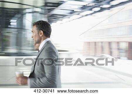 Stock Image - Corporate businessman with coffee walking outdoors. Fotosearch