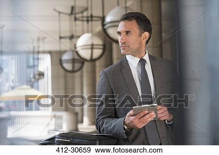Stock Photo - Corporate businessman with digital tablet looking away. Fotosearch