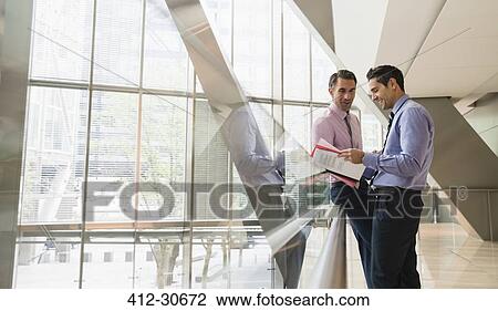 Corporate businessmen discussing paperwork in modern lobby View Large Photo Image Stock Image - Corporate businessmen discussing paperwork in modern lobby. Fotosearch