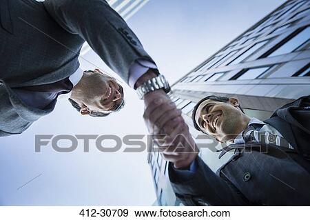 Stock Photo - Corporate businessmen handshaking below building. Fotosearch
