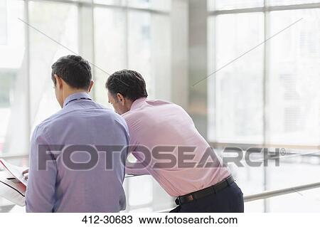 Corporate businessmen reviewing paperwork at railing in office View Large Photo Image Stock Image - Corporate businessmen reviewing paperwork at railing in office. Fotosearch