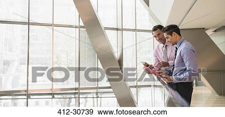 Corporate businessmen using digital tablet at railing in office View Large Photo Image Stock Photo - Corporate businessmen using digital tablet at railing in office. Fotosearch