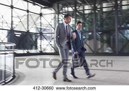 Stock Image - Corporate businessmen walking in modern lobby. Fotosearch