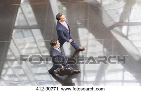 Corporate businessmen walking in modern office lobby View Large Photo Image Stock Image - Corporate businessmen walking in modern office lobby. Fotosearch