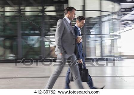 Stock Image - Corporate businessmen with coffee walking outside building. Fotosearch