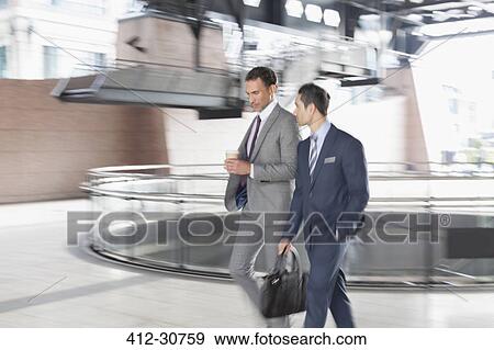 Stock Photo - Corporate businessmen with coffee walking and talking. Fotosearch