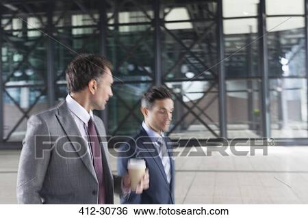 Stock Photograph - Corporate businessmen with coffee walking and talking outside building. Fotosearch