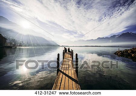 Stock Photo - Couple at the edge of dock over sunny tranquil lake, Switzerland. Fotosearch