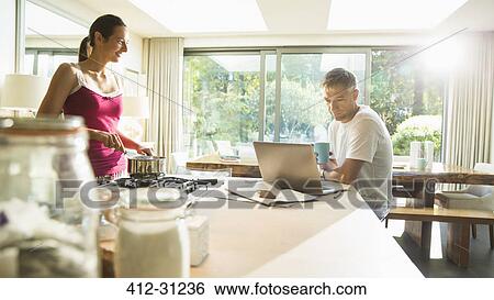 Couple cooking and working at laptop in morning kitchen View Large Photo Image Stock Photograph - Couple cooking and working at laptop in morning kitchen. Fotosearch