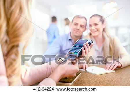 Picture - Couple paying for jewelry watching jeweler using credit card reader. Fotosearch