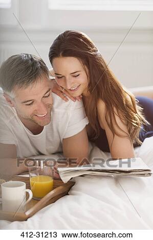 Stock Image - Couple reading newspaper in bed. Fotosearch