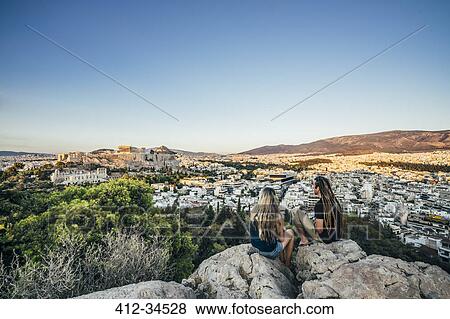 Stock Photo - Couple sitting on rocks overlooking landscape, Athens, Greece. Fotosearch
