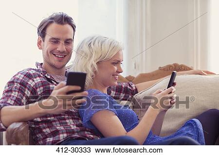 Couple texting with cell phones on living room sofa View Large Photo Image Stock Image - Couple texting with cell phones on living room sofa. Fotosearch