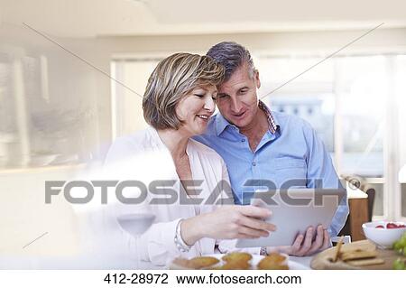 Stock Image - Couple using digital tablet in kitchen. Fotosearch
