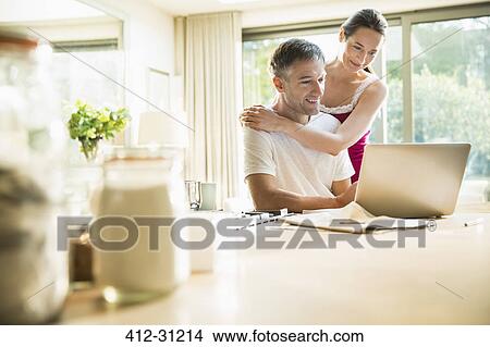 Picture - Couple using laptop in morning kitchen. Fotosearch