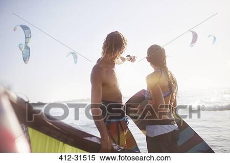 Stock Photography - Couple watching kiteboarders over sunny ocean. Fotosearch