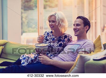 Couple watching TV and eating popcorn on living room sofa View Large Photo Image Stock Image - Couple watching TV and eating popcorn on living room sofa. Fotosearch