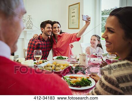 Couple with camera phone taking selfie at Christmas dinner table View Large Photo Image Stock Image - Couple with camera phone taking selfie at Christmas dinner table. Fotosearch