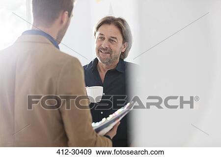 Stock Photo - Creative businessmen drinking coffee and talking in office. Fotosearch