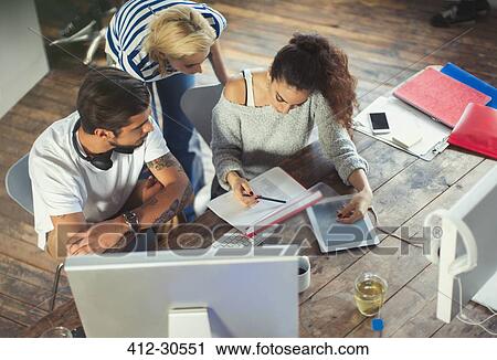 Stock Image - Creative young business people discussing paperwork in office. Fotosearch