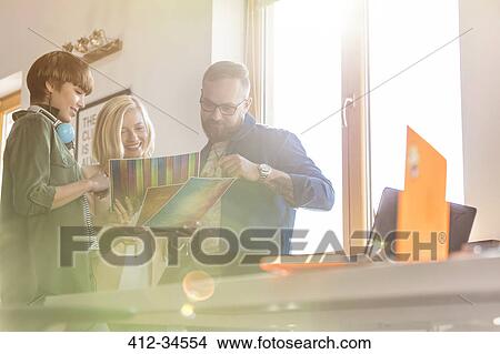 Picture - Design professionals reviewing proofs in sunny office. Fotosearch