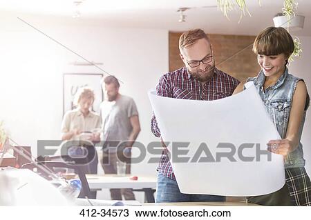 Stock Image - Design professionals reviewing blueprints in office. Fotosearch