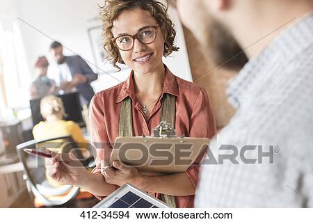 Design professionals with clipboard talking in office View Large Photo Image Picture - Design professionals with clipboard talking in office. Fotosearch
