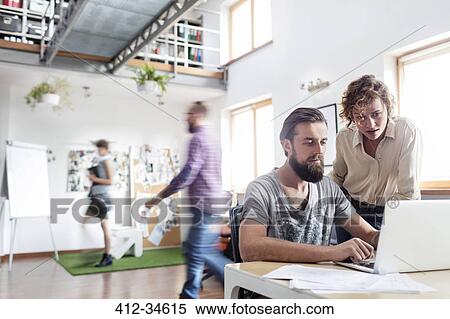 Stock Photography - Design professionals working at laptop in office. Fotosearch