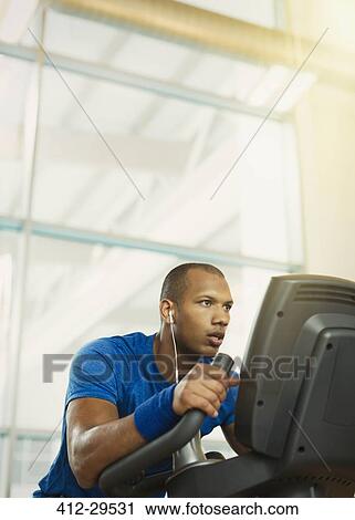 Stock Image - Determined man on elliptical trainer at gym. Fotosearch