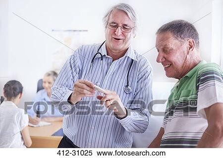 Stock Photography - Doctor showing senior man digital thermometer at checkup. Fotosearch