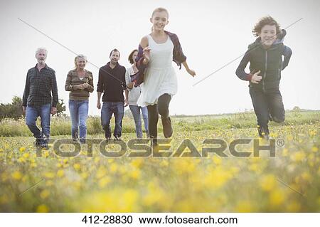 Stock Image - Energetic brother and sister running in meadow with family in background. Fotosearch
