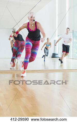 Stock Image - Energetic fitness instructor leading aerobics class. Fotosearch