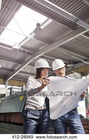 Stock Photo - Engineers reviewing blueprints in factory. Fotosearch