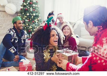 Stock Photo - Enthusiastic friends exchanging Christmas gifts. Fotosearch