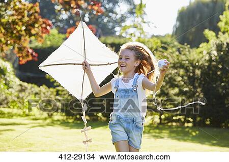 Picture - Enthusiastic girl running with kite in sunny garden. Fotosearch