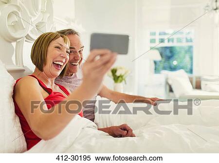 Stock Photography - Enthusiastic mature a couple taking selfie in bed. Fotosearch
