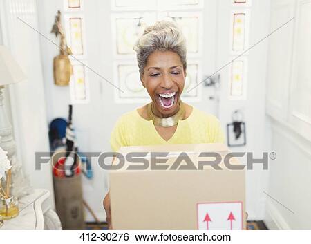 Stock Photograph - Enthusiastic mature woman receiving package in foyer. Fotosearch