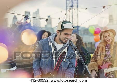 Enthusiastic musician playing guitar and singing at rooftop party View Large Photo Image Stock Image - Enthusiastic musician playing guitar and singing at rooftop party. Fotosearch