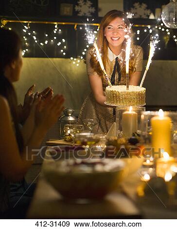 Stock Photo - Enthusiastic woman serving cake with sparkler fireworks to clapping friends. Fotosearch