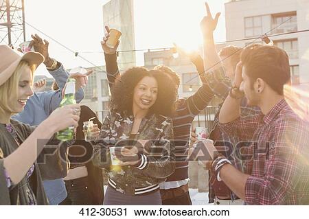 Enthusiastic young adult friends dancing and drinking at rooftop party View Large Photo Image Stock Image - Enthusiastic young adult friends dancing and drinking at rooftop party. Fotosearch