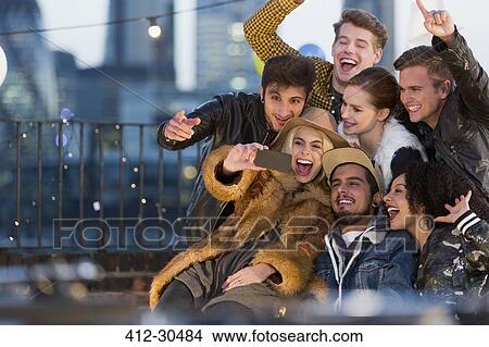 Picture - Enthusiastic young adult friends taking selfie at rooftop party. Fotosearch